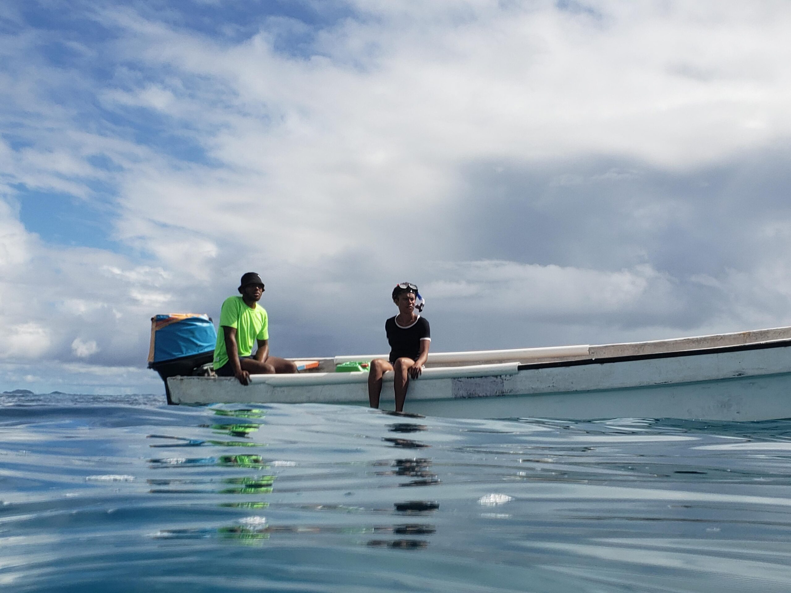 Water view of boat in Fiji, with two people sat on edge, looking into distace