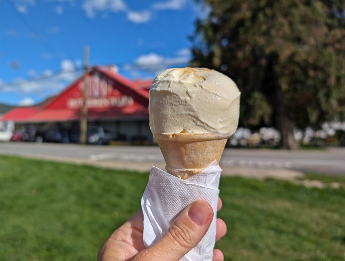 Close up of ice cream cone in front of bright red barn like D Dutchmen Dairy building in Sicamous, BC
