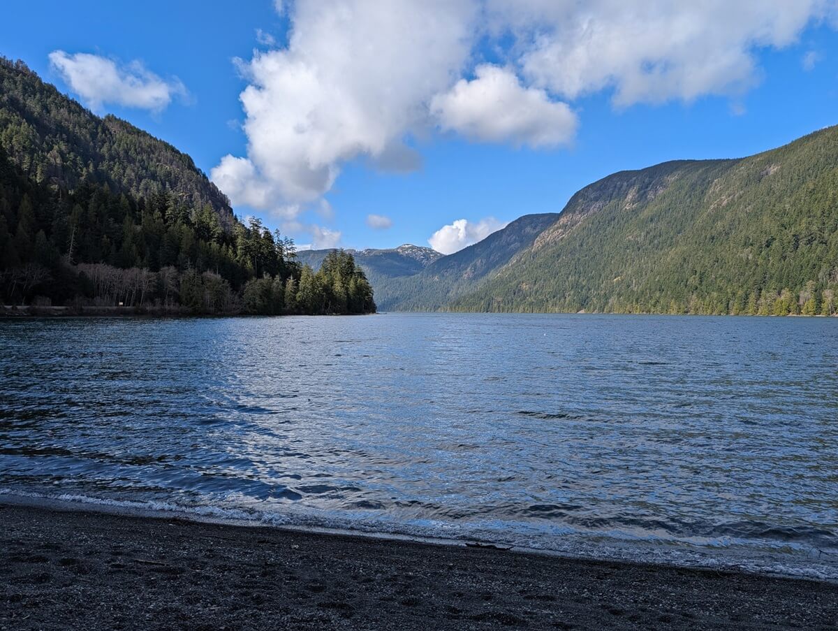 Beach view of Cameron Lake, which is fairly calm and surrounded by fairly steep forested mountains