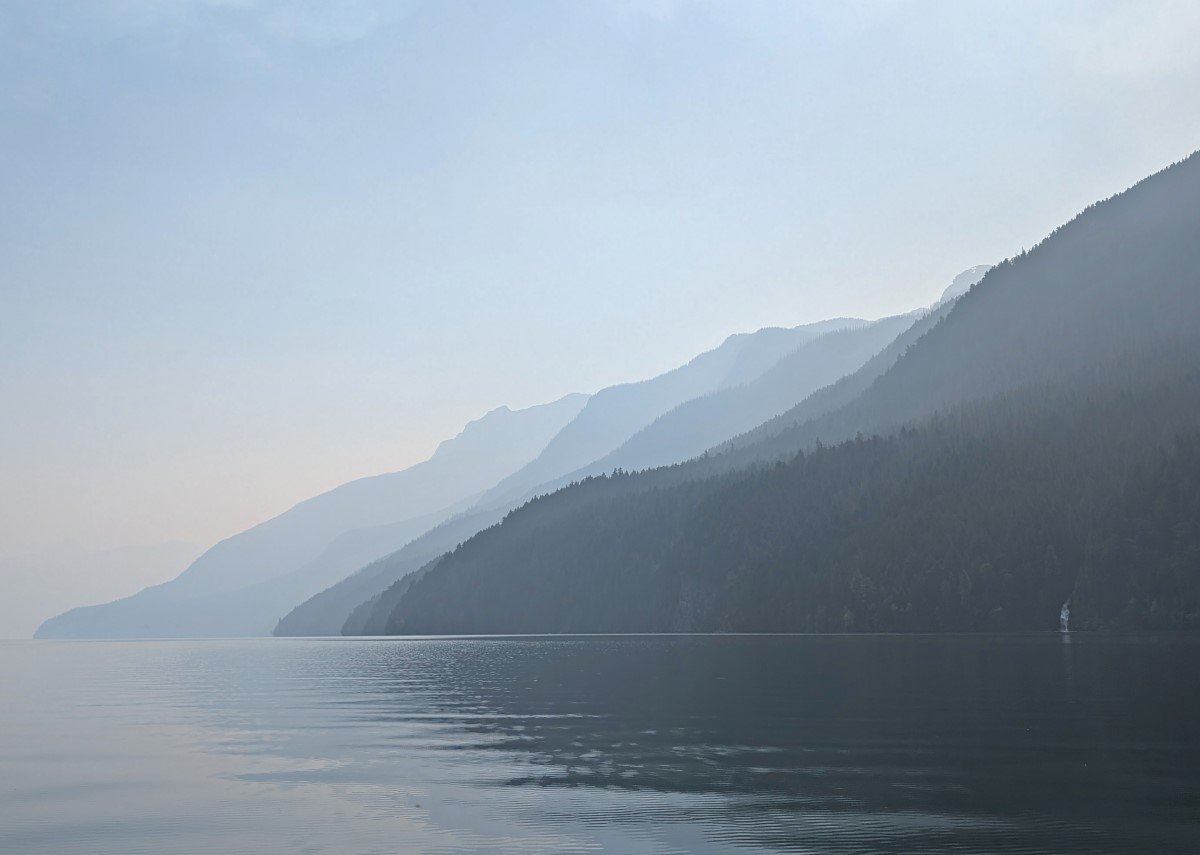 Smoky view on calm lake with layers of mountains in distance