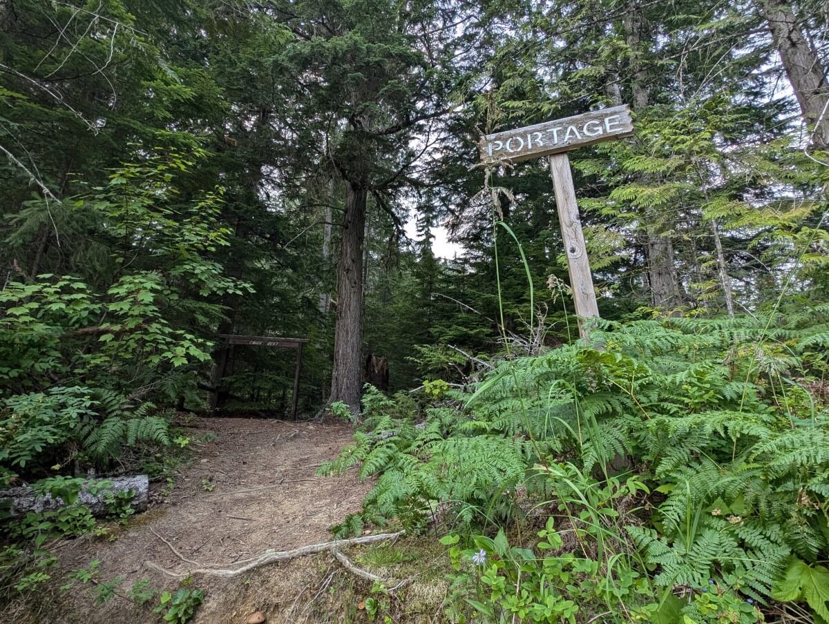 Shore view looking up to Clearwater river portage with wooden portage sign, wooden rack and backdrop of trees