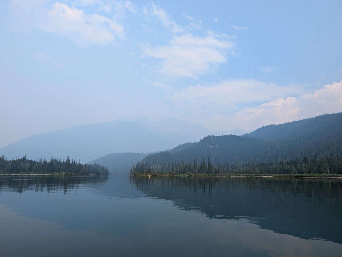Canoe view of calm, reflective Clearwater Lake with forested shoreline and smoky skies