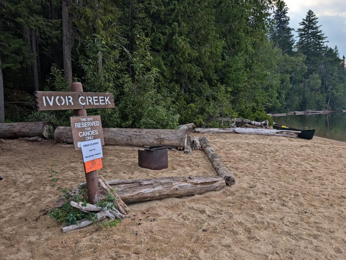 Sandy beach with Ivor Creek sign, driftwood and trees in background