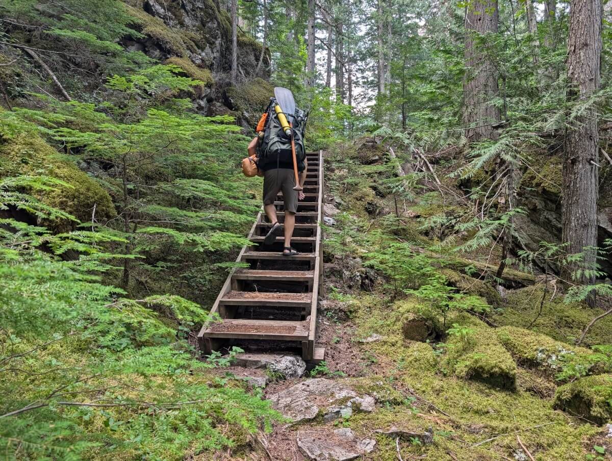 JR portages a canoe on his head up a set of wooden stairs in the forest between Clearwater and Azure lakes