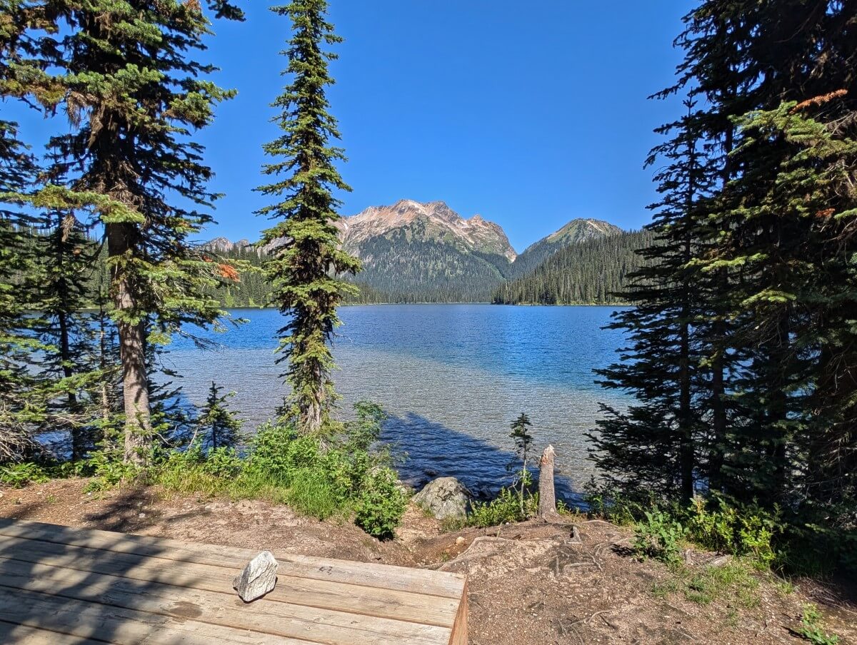 Edge of wooden tent pad next to Big Peters Lake, which is backdropped by mountain range