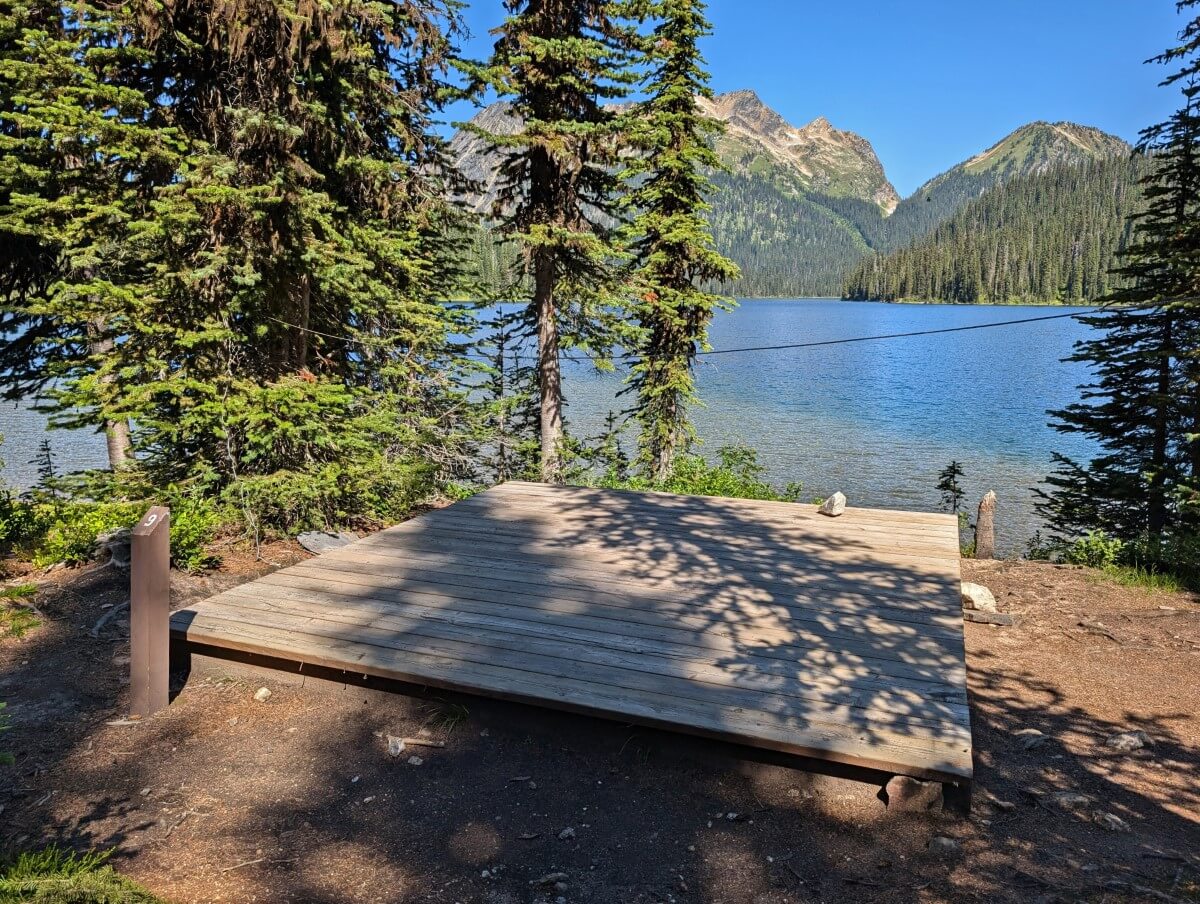 Wooden tent pad (number 9) in front of Big Peters Lake, with mountain peaks behind
