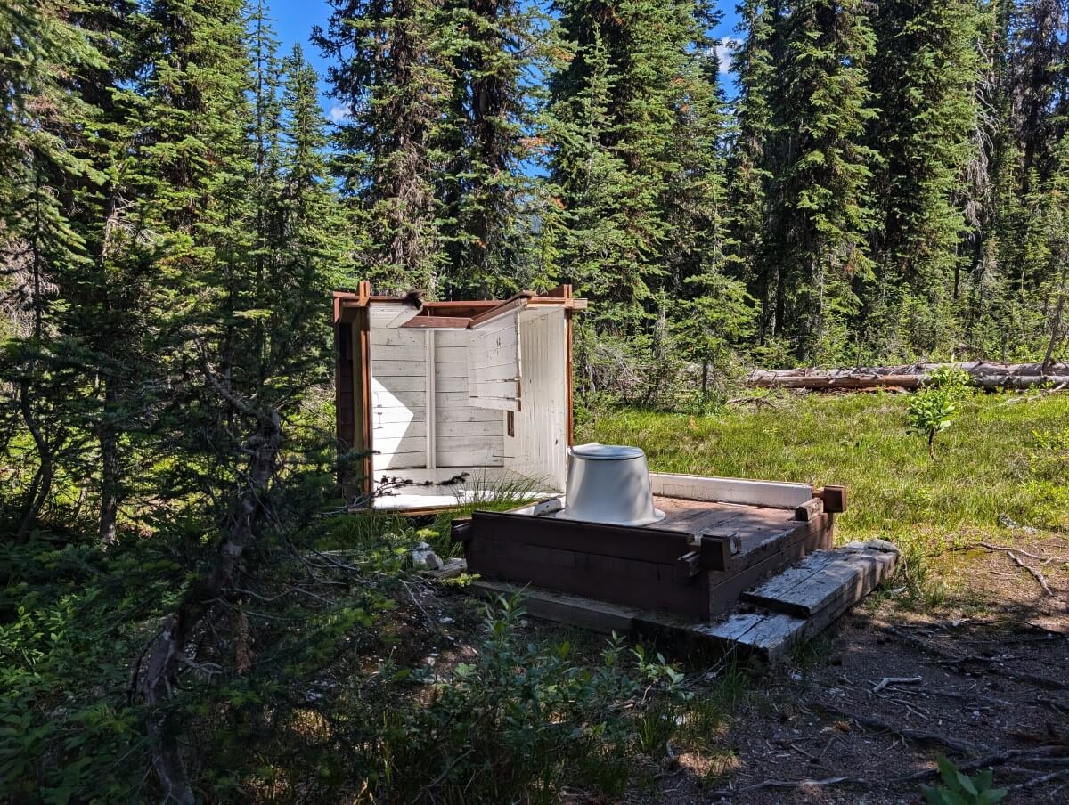 Broken outhouse in Big Peters Lake Campground - the roof of the wooden building has separated from the bottom. The plastic toilet seat is still visible