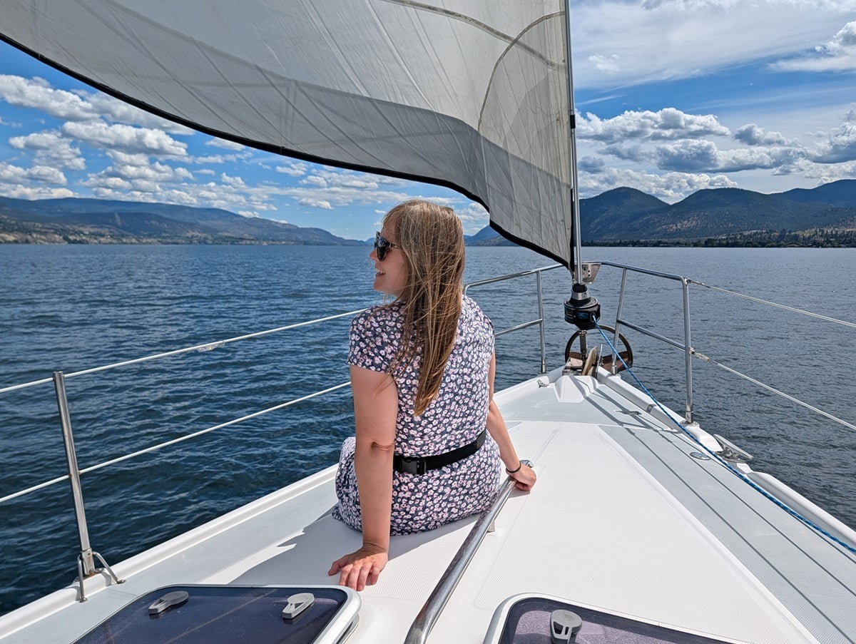 Back view of Gemma sat on the deck of a yacht on Okanagan Lake, with calm water and forested mountains behind