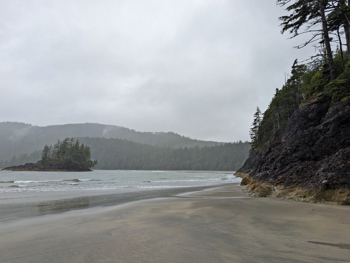 Side view of headland at San Josef Bay, with the ocean rolling up to the edge. There is an island just offshore