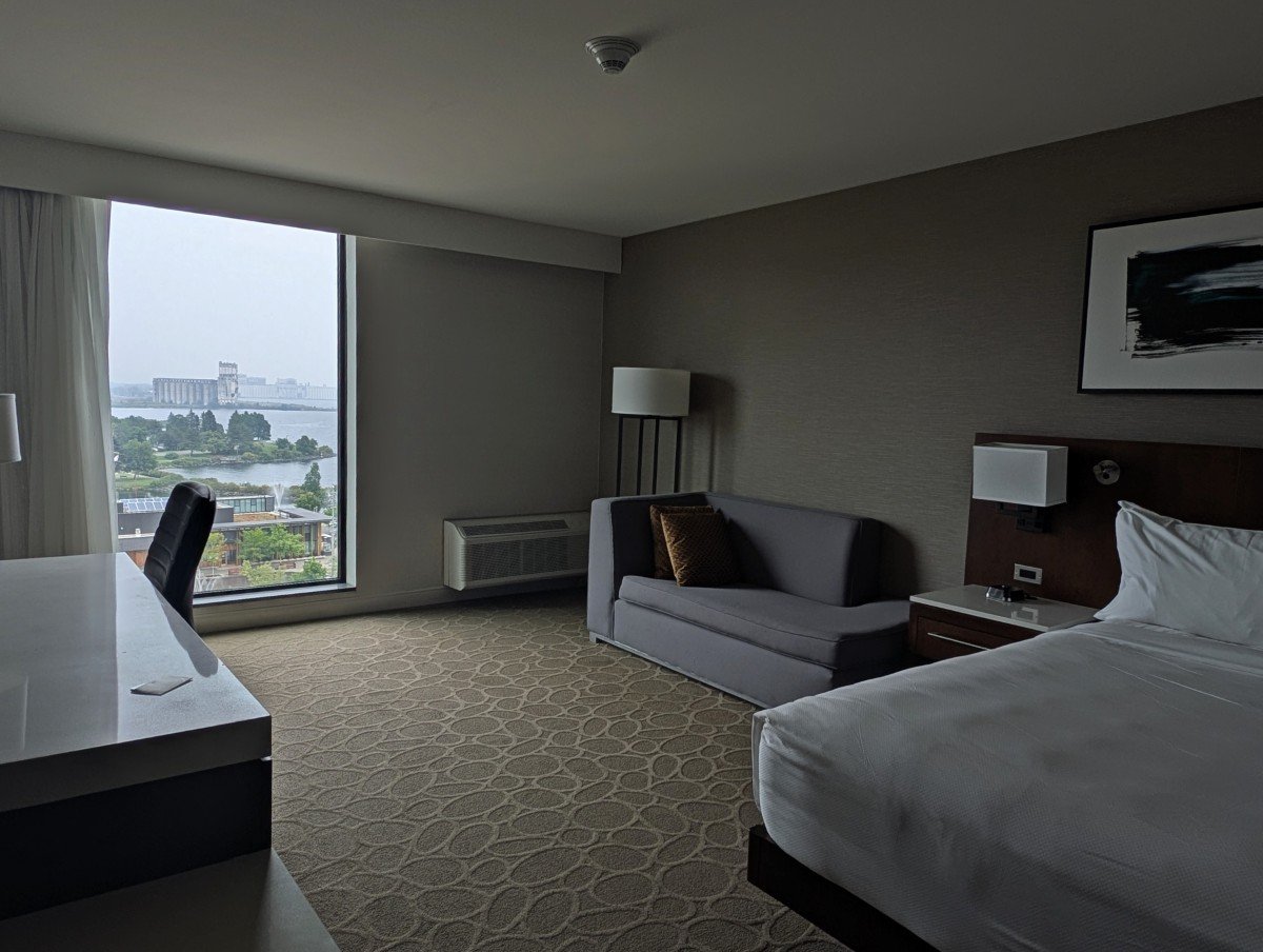 Delta Hotel room in Thunder Bay with king bed on right, couch and large floor to ceiling windows with lake view