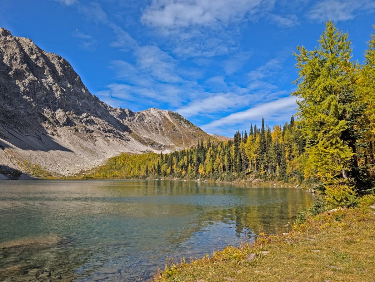 Calm Diana Lake from lakeshore, lined by trees and backdropped by high mountains