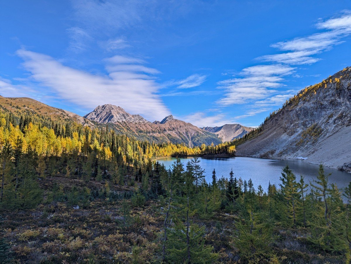 Looking down on Diana Lake from higher trail, the foreground of which is in shadow and the far end is lined by golden larch trees, lit up by the sun