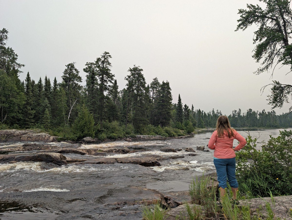Back view of Gemma standing on shore looking out at rapids in Wabakimi Provincial Park
