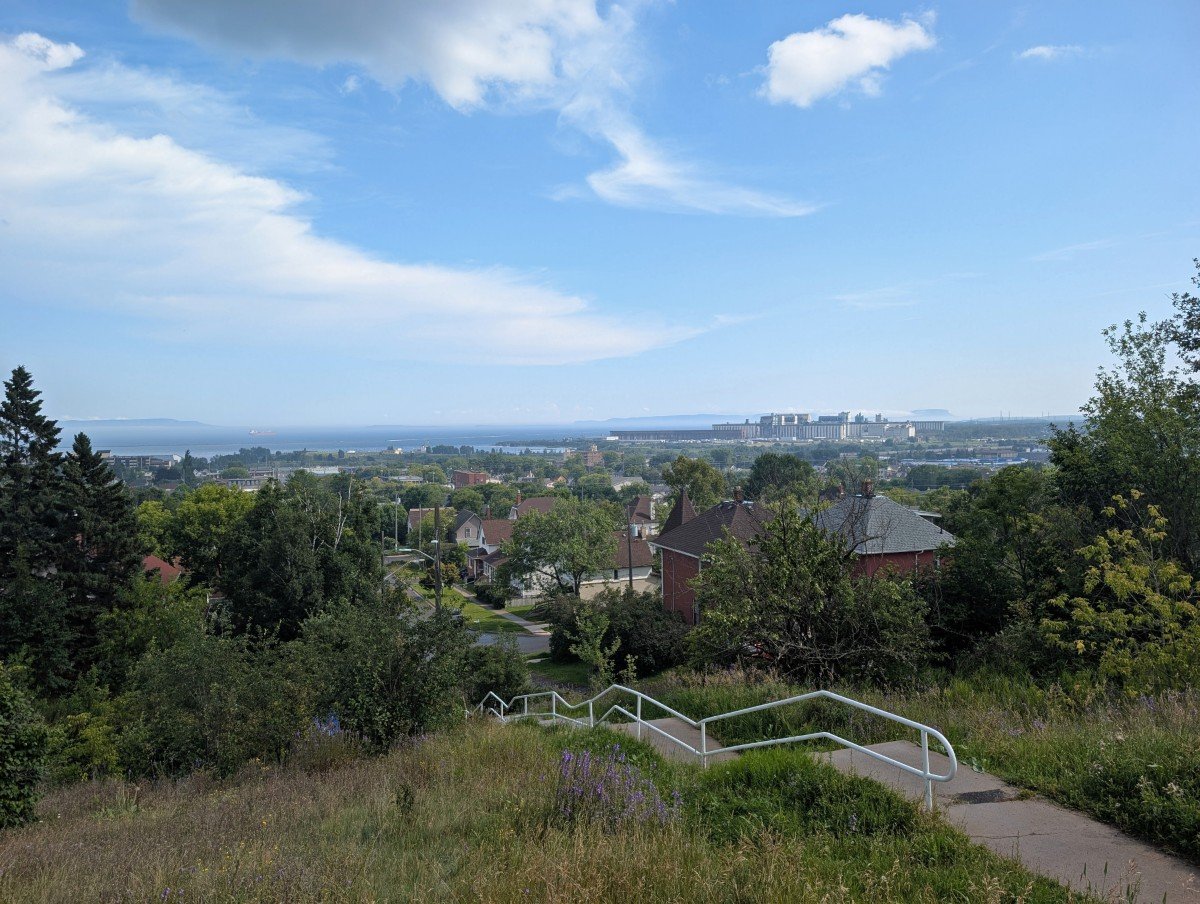 Stairs leading through the flower filled grassy sloped area of Hillcrest Park in Thundery Bay, with lake and industrial area views in background