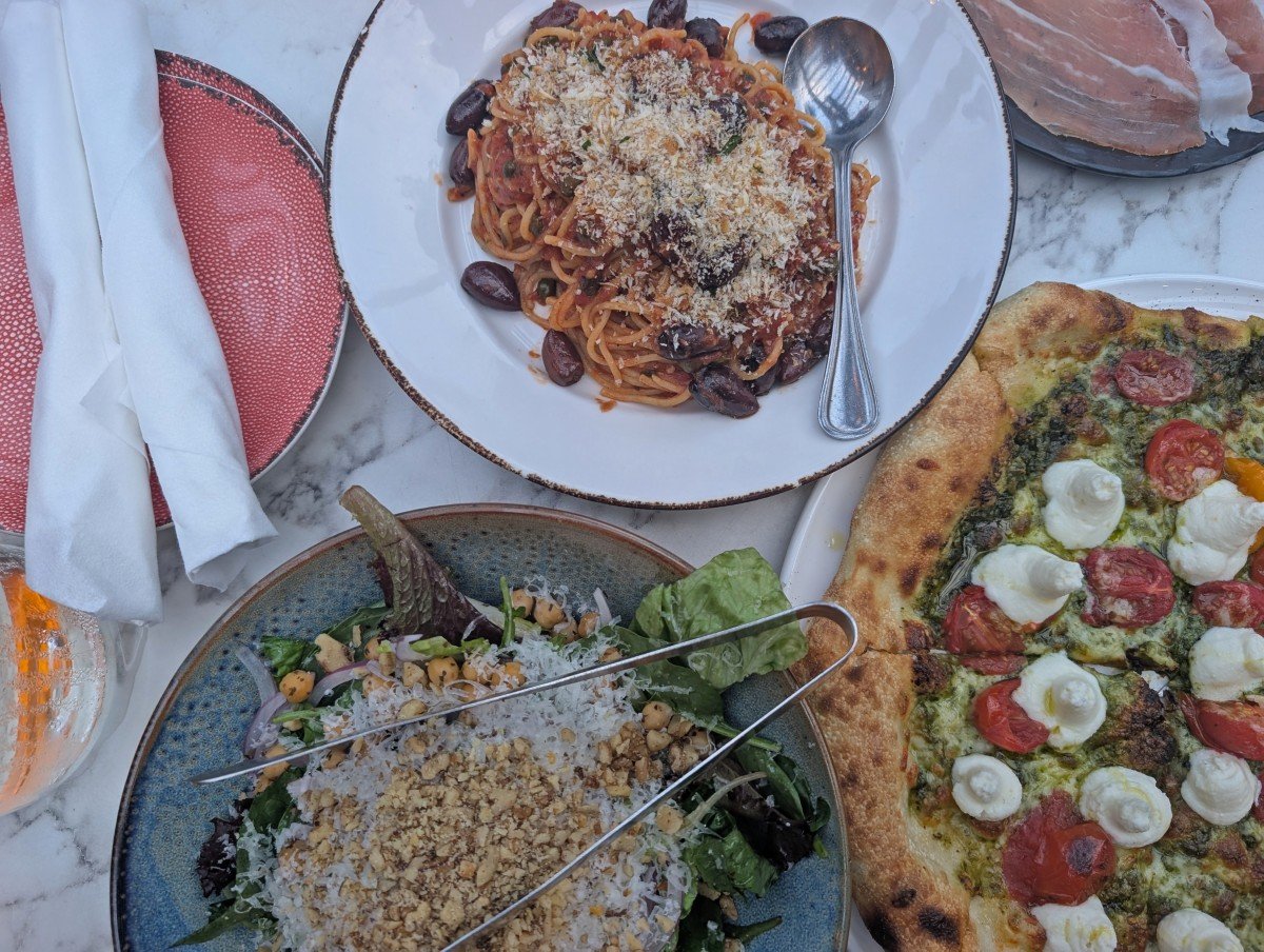 Overhead view of three dishes at the Nook restaurant in Thunder Bay - pasta, salad and pizza