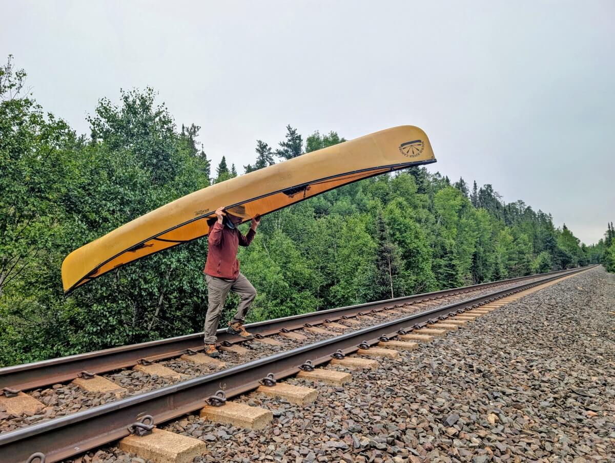 JR carries a yellow canoe over railway tracks in Wabakimi Provincial Park