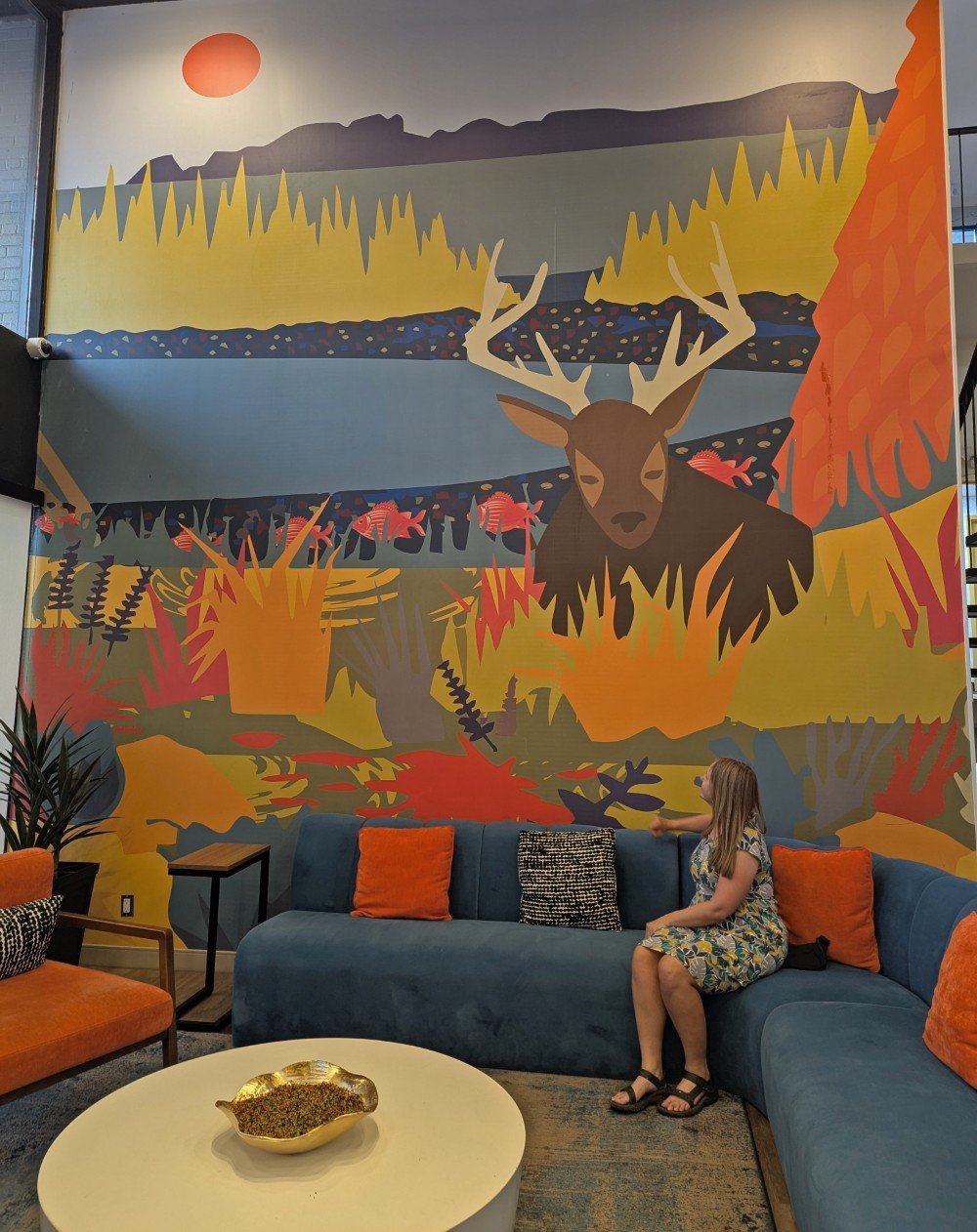 Gemma sits on a couch in front of a colourful Thunder Bay mural at the Superior Shores Hotel in Thunder Bay