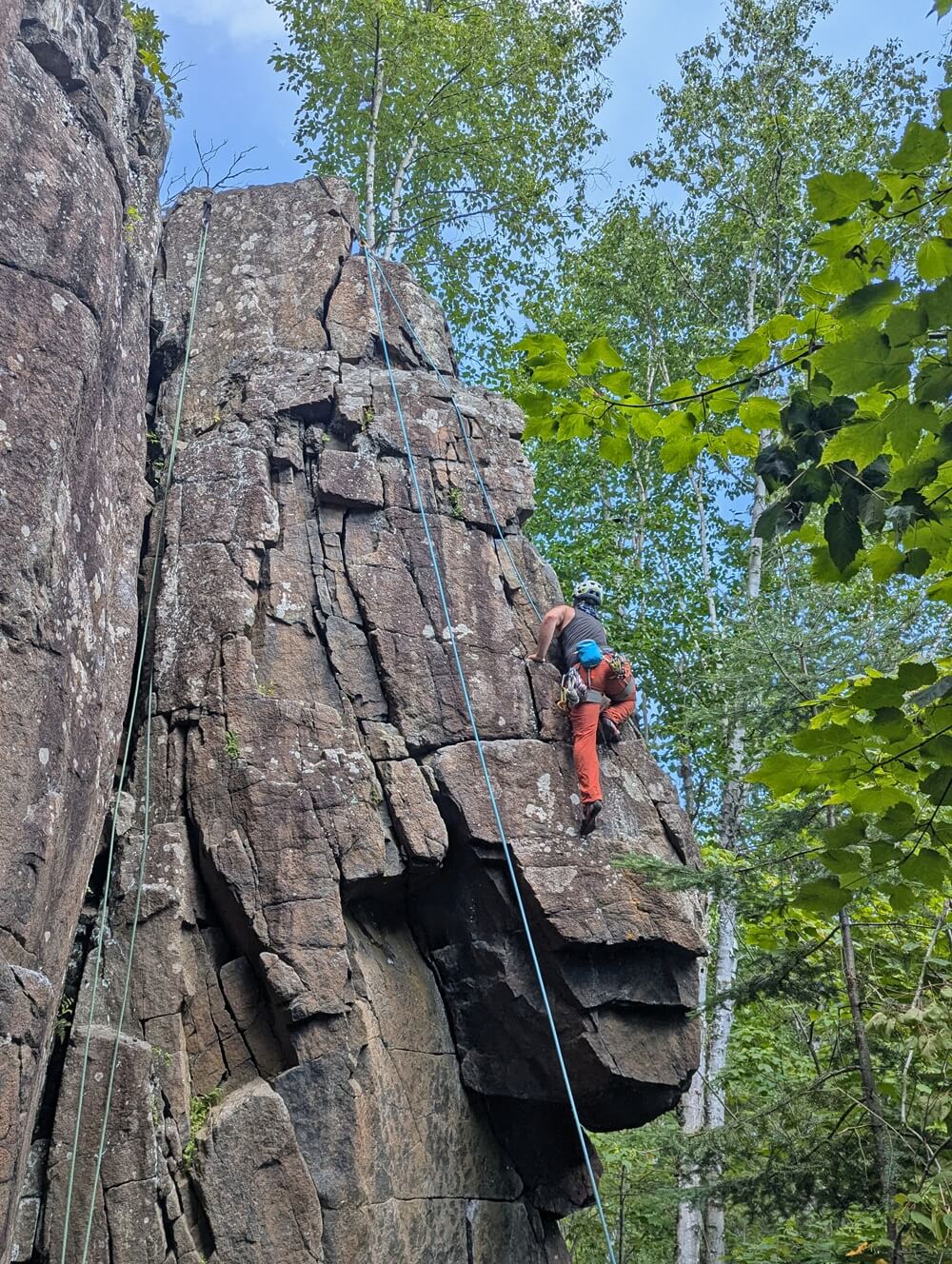 Rock climber ascends a rugged pillar of rock at the Bluffs climbing area in Thunder Bay
