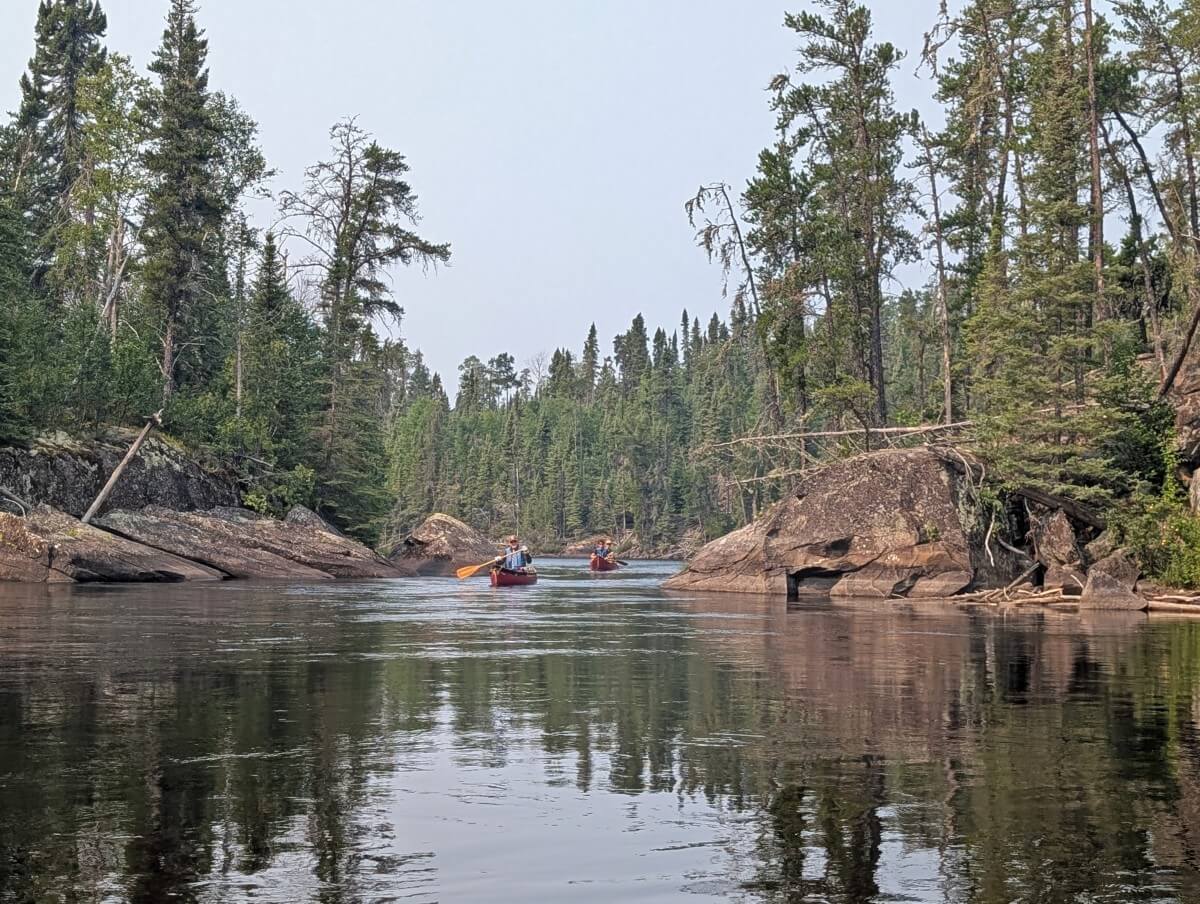 Two red canoes approach through narrow river section in Wabakimi Provincial Park
