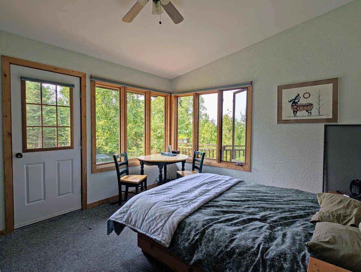 Wabakimi Outfitters Lodge room, featuring double bed, two seats, table and large corner windows