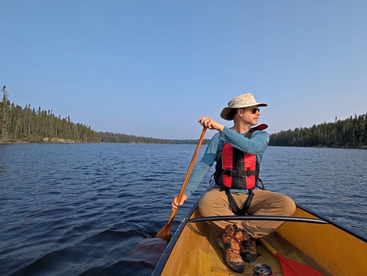 A canoeist sits in a yellow canoe with a paddle in the water on a sunny day