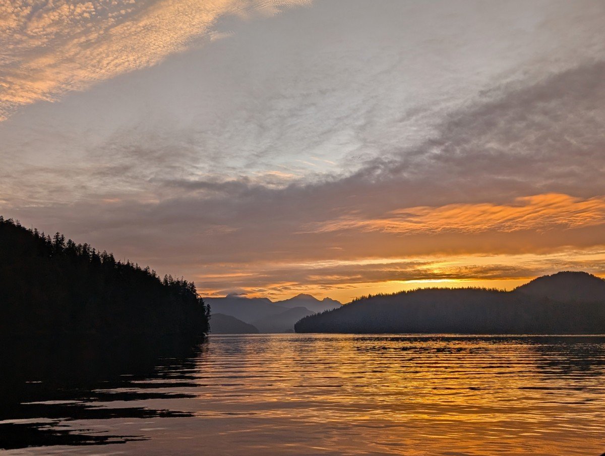 Sunrise view on Zodiac boat tour in Tofino, with orange colours behind layers of mountains and islands