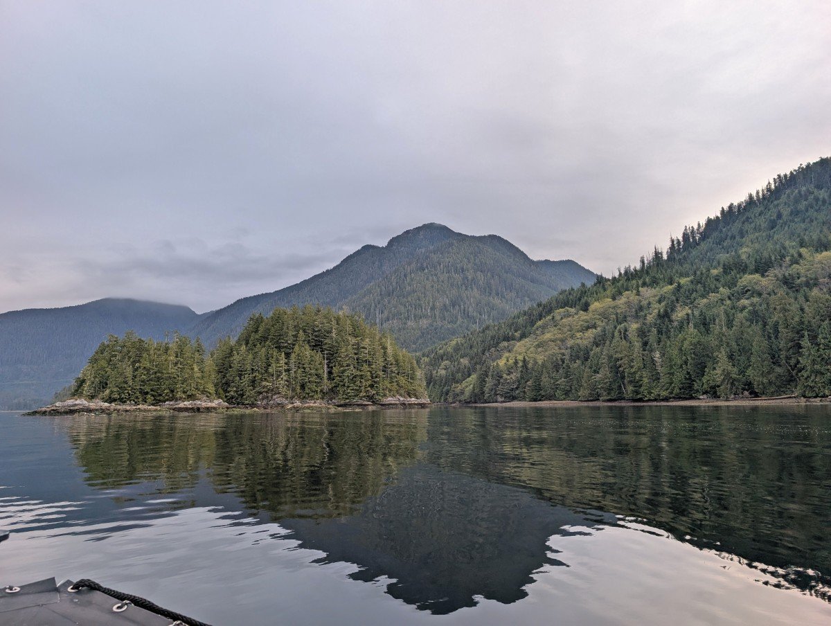 Clayoquot Sound view from Zodiac boat, with reflective ocean providing mirror views of forested islands, mountains and grey skies