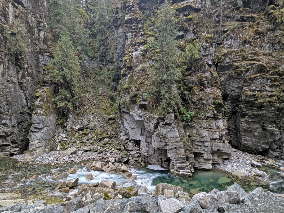 Looking across rocks to turquoise coloured Coquihalla River, with eroded canyon walls above, some sections covered in moss
