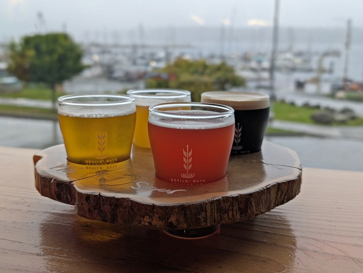 Close up of colourful beer flight at Devils' Bath Brewing Co in Port McNeill, placed in front of a window that has views of the marina and ocean