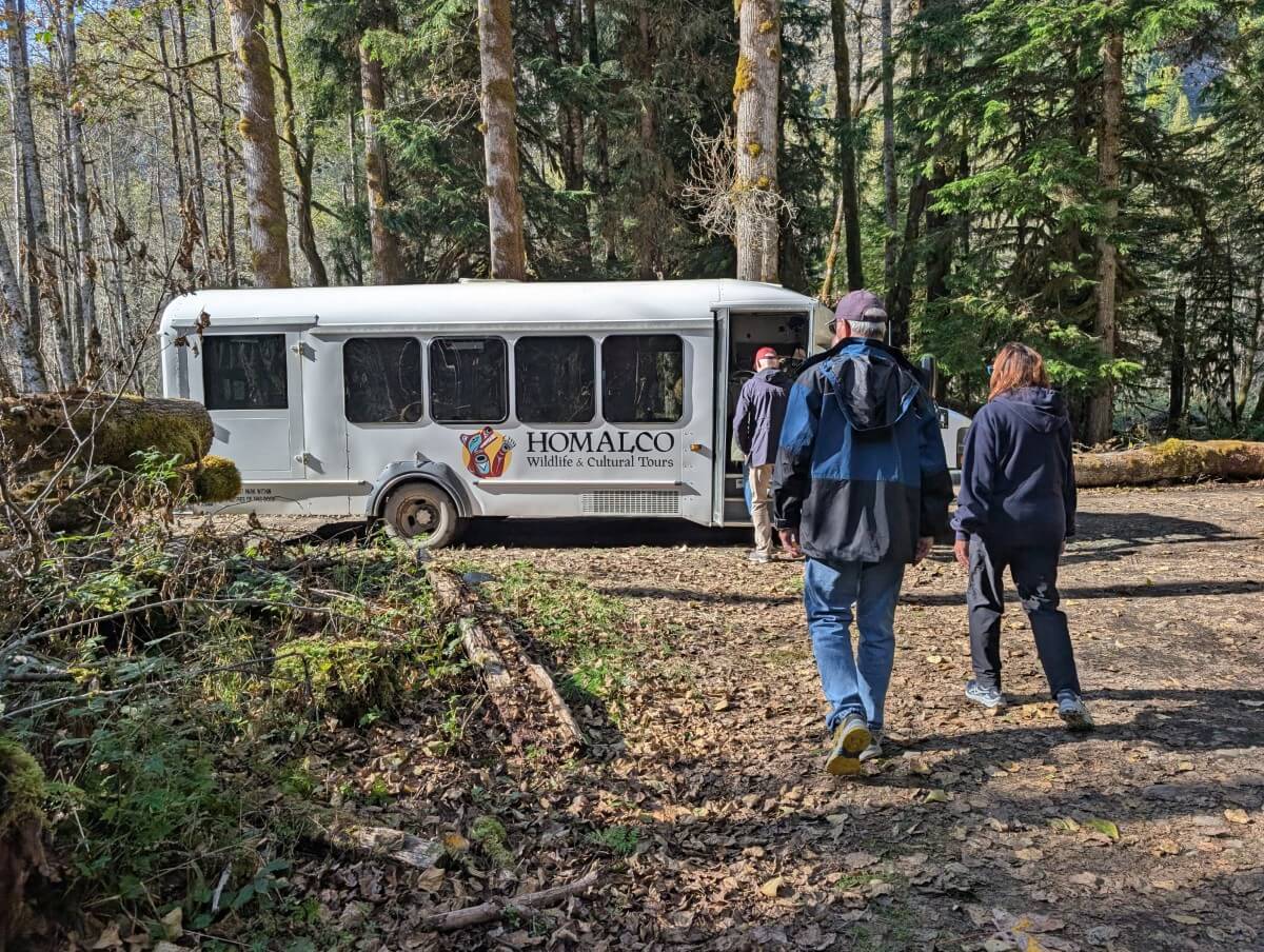 Back view of tour group members returning to small white Homalco Wildlife and Cultural Tours bus in forested area
