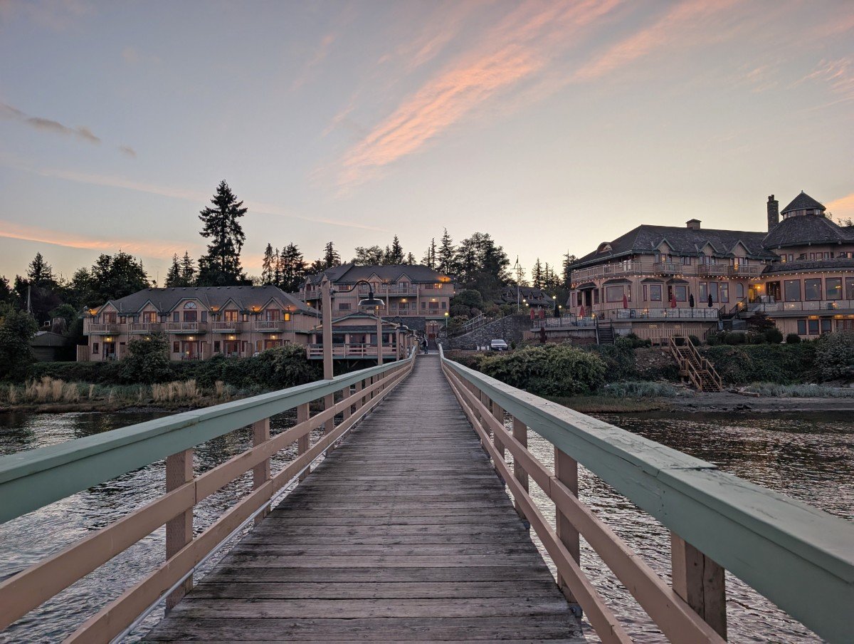Boardwalk view of Painter's Lodge hotel property in Campbell River, with large bar/restaurant on right and two separate accommodation buildings on left. Sunset colours in the sky