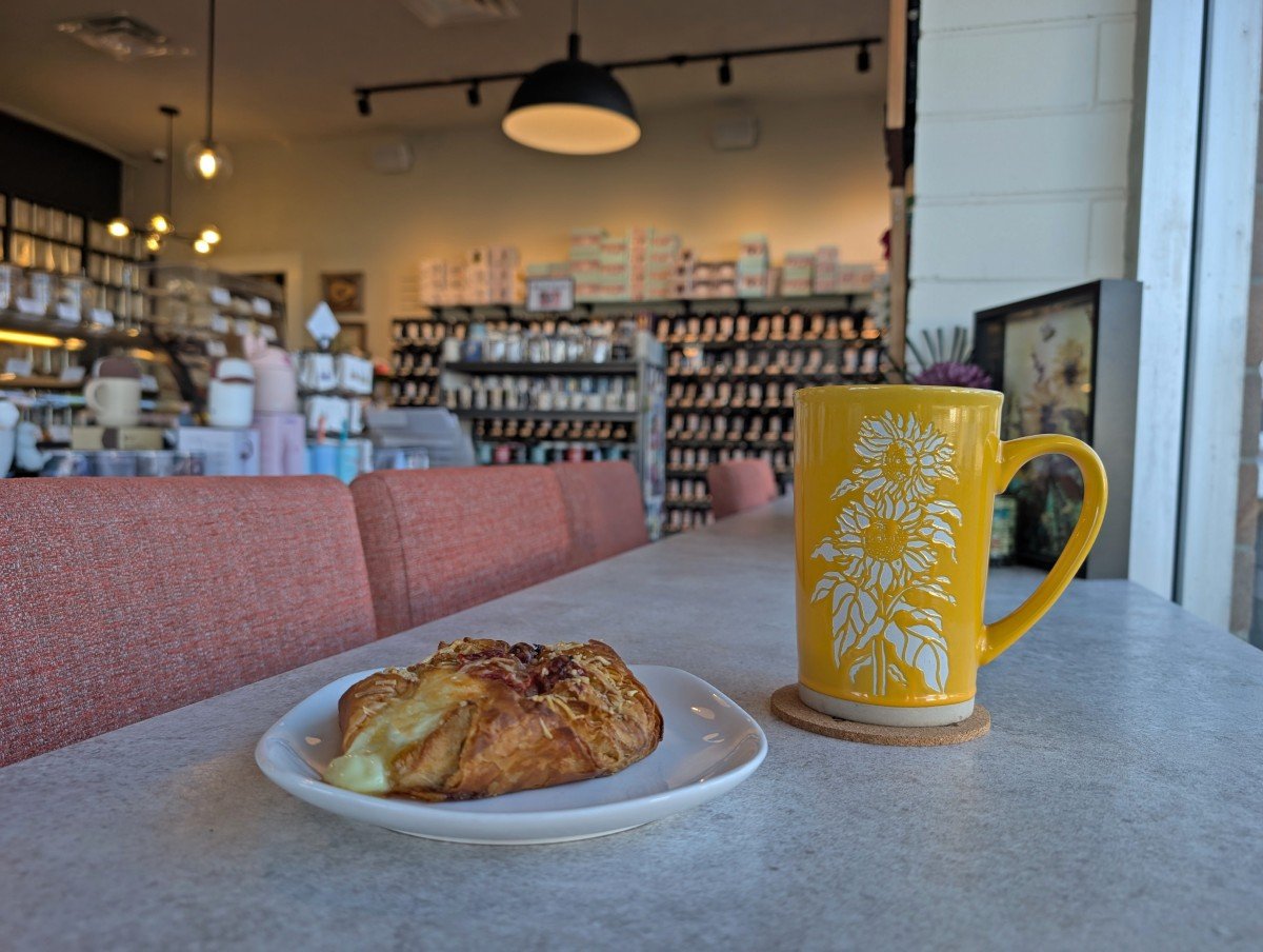 Close up of yellow and white mug with pastry in Stonehouse Teas cafe in Campbell River, with racks of tea behind