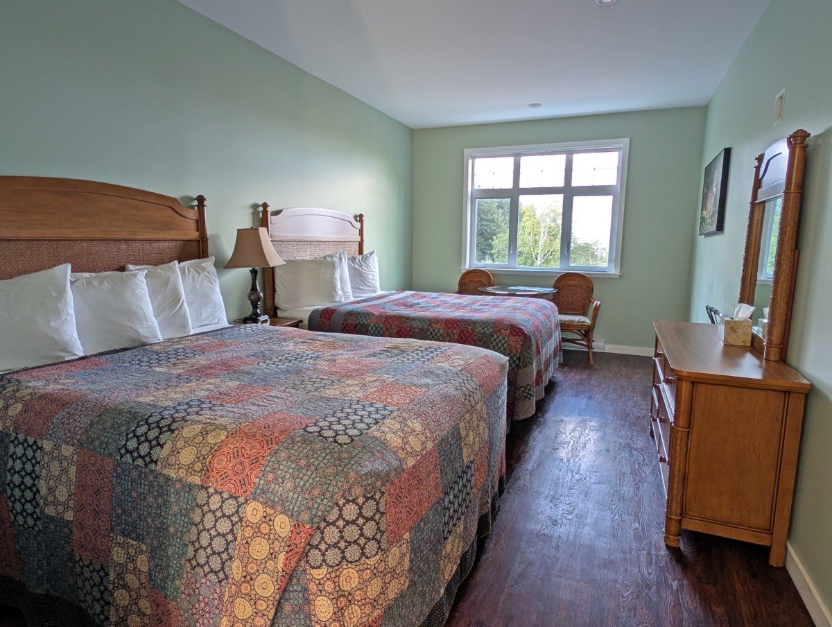 Telegraph Cove Resort hotel room with two queens, pattern bedspread, dresser and two chairs and table