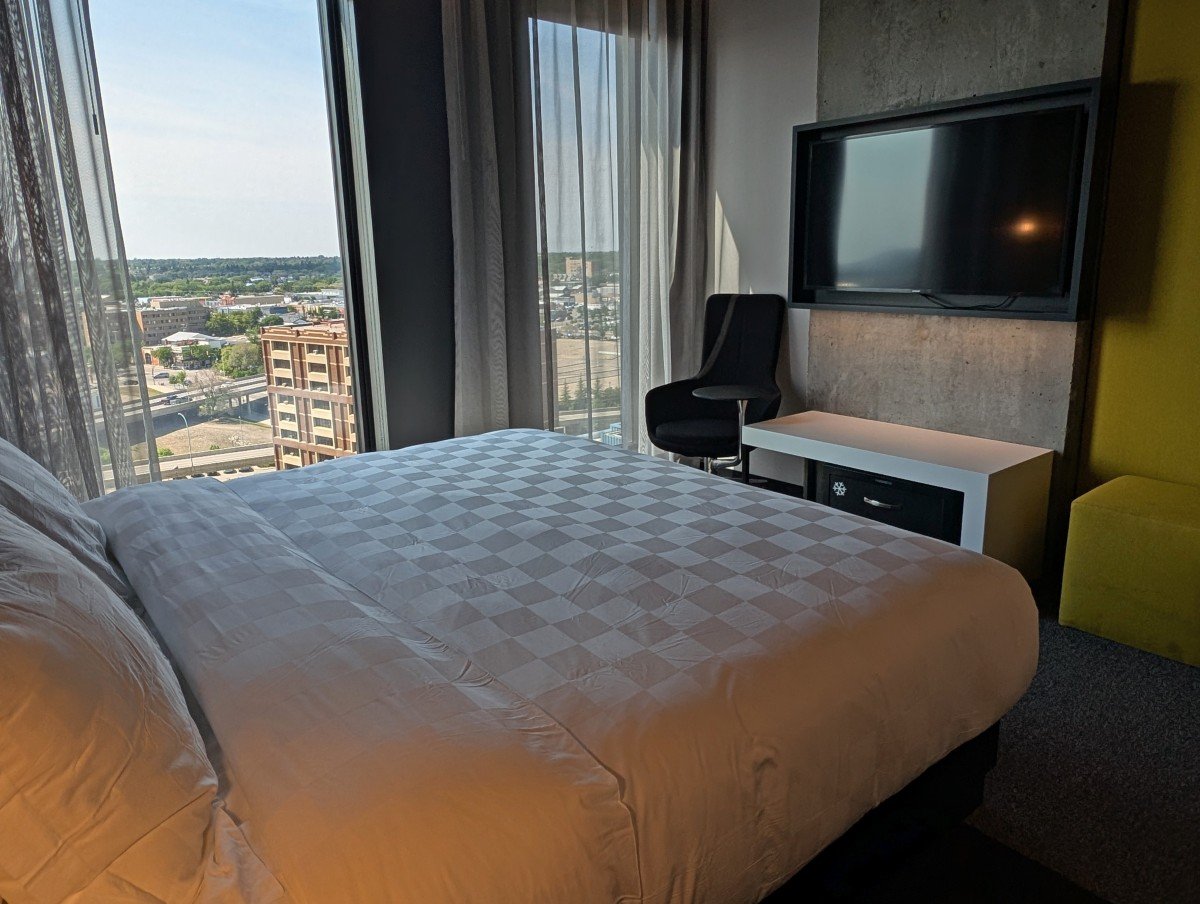 Alt Hotel room with large bed and television, side chair and floor to ceiling windows