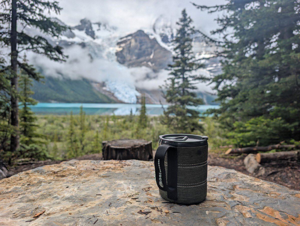 Close up of green Infinity mug on log table in front of Berg Lake view at campground