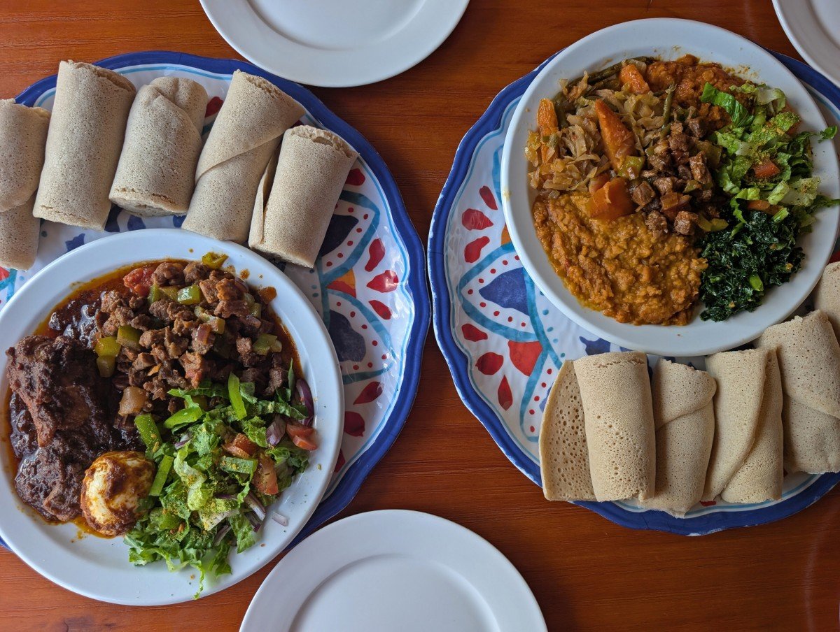 Overhead view of an Eritrean meal at Dahlak restaurant in Saskatoon, featuring two dishes with a variety of stews and salad, on colourful plates with rolled injera flatbread on the side