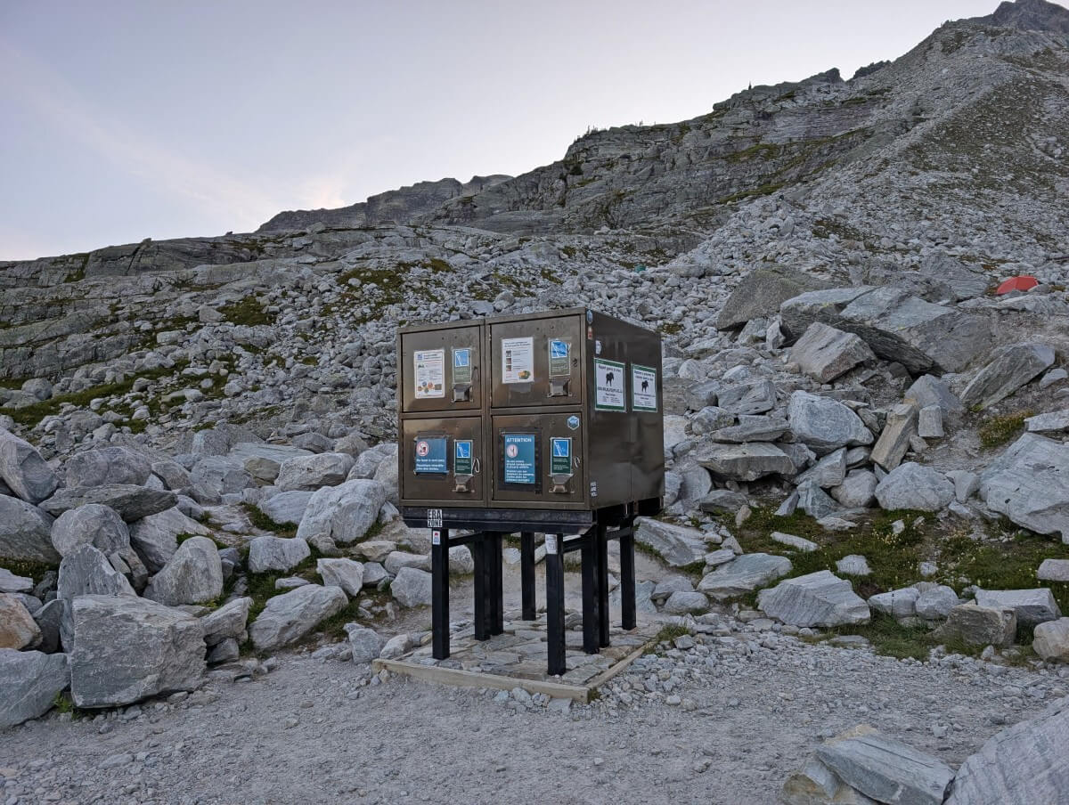 Close up of metal food caches at Hermit Meadows campground - a large metal box with four separate areas. The caches sit in a cleared area surrounded by rocks