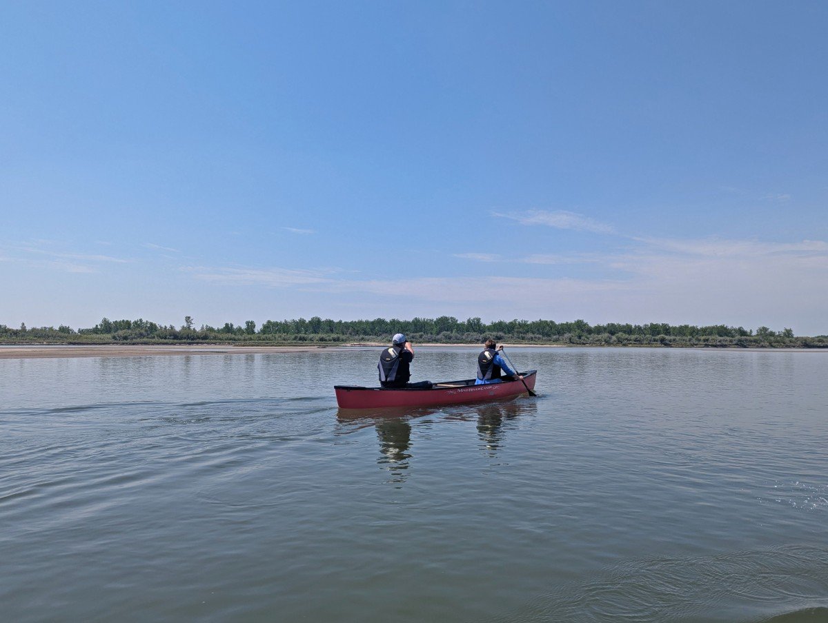 Canoe view looking over to red canoe with two paddlers on the South Saskatchewan River