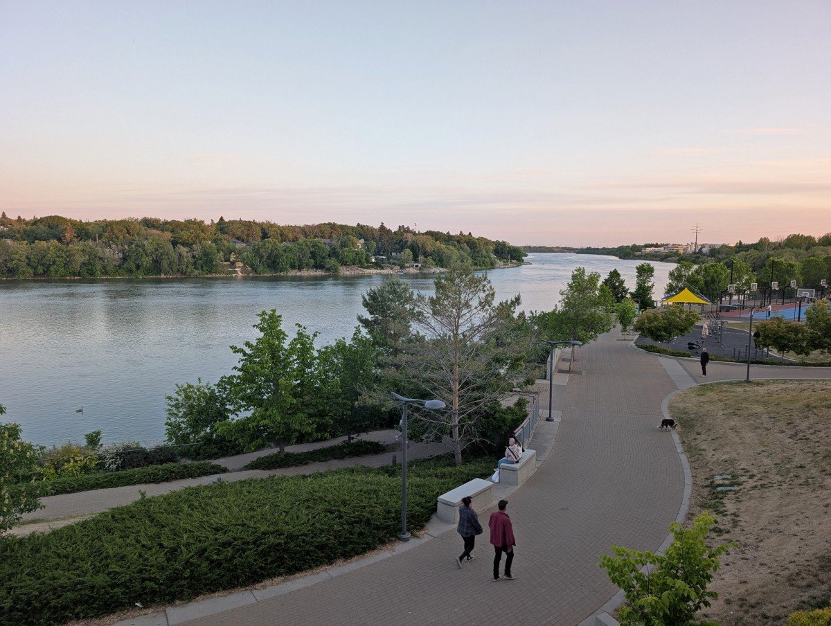 Looking down on people walking along the Meewasin Trail in Saskatoon, next to the South Saskatchewan River, which is lined by trees