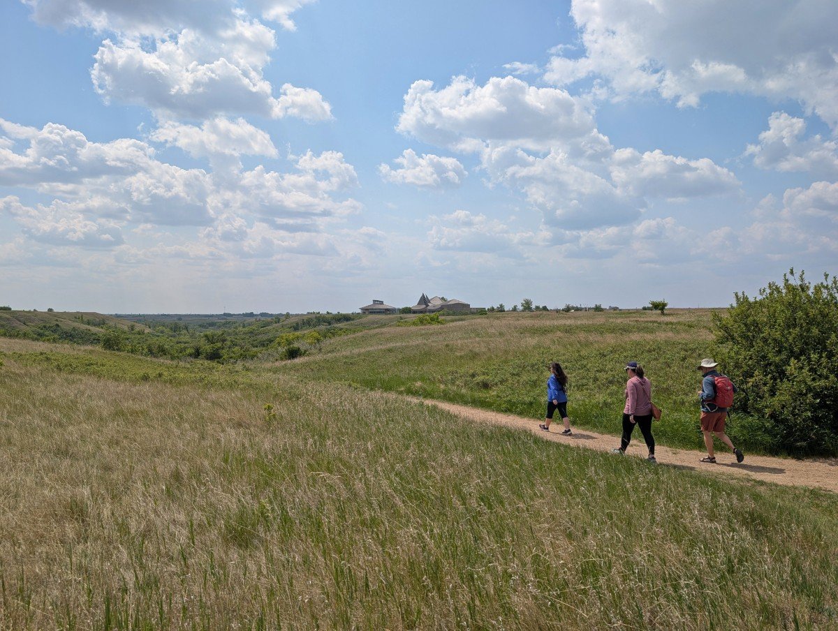 Three hikers walk on dirt path surrounded by grassland at Wanuskewin in Saskatoon