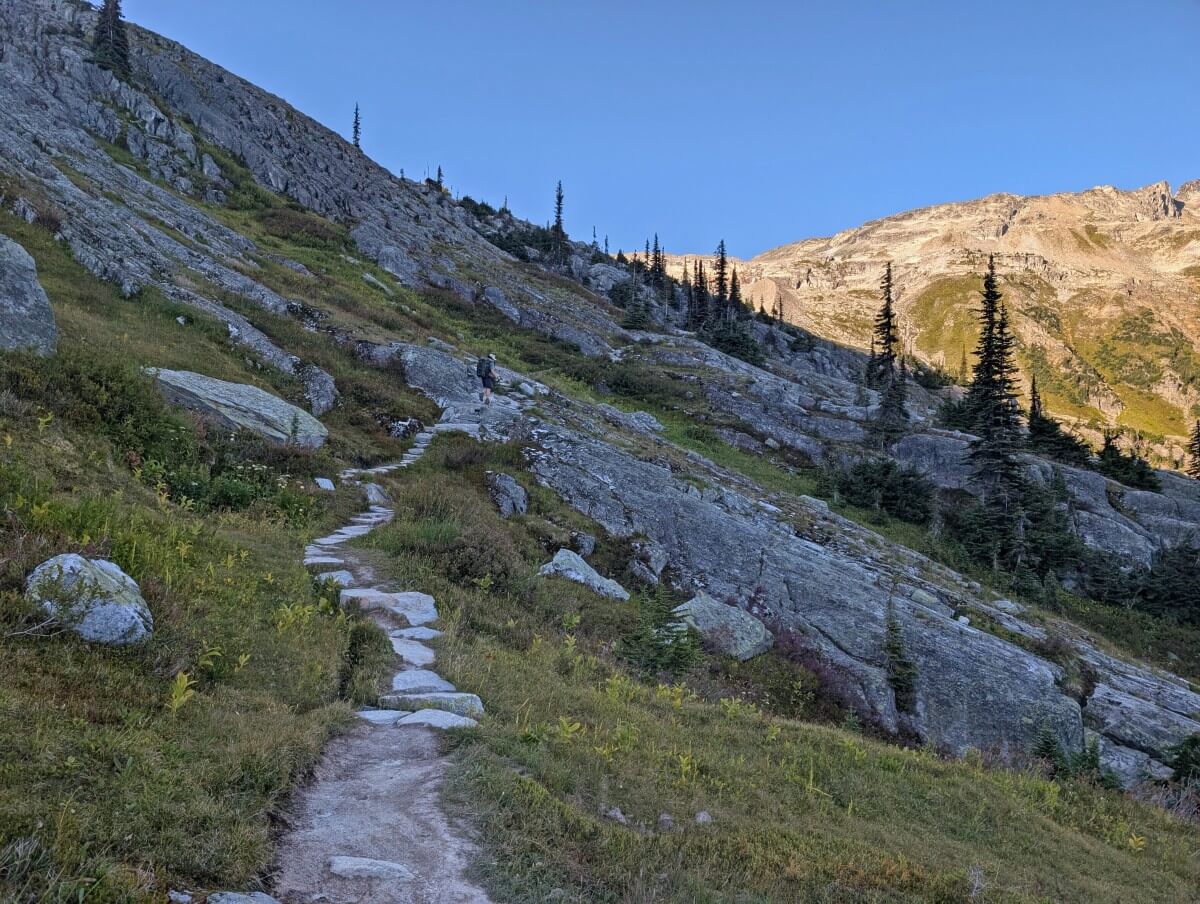 Looking ahead to well built dirt and rock pathway through alpine meadows, traversing a slope