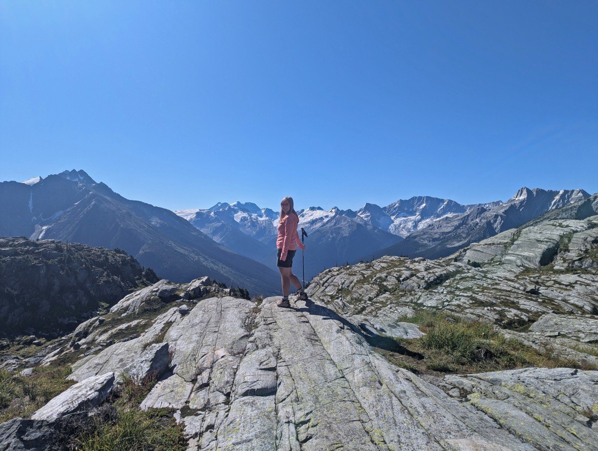 Back view of hiker turning around to pose in front of snow capped mountain view at the end of the Hermit Trail, Glacier National Park