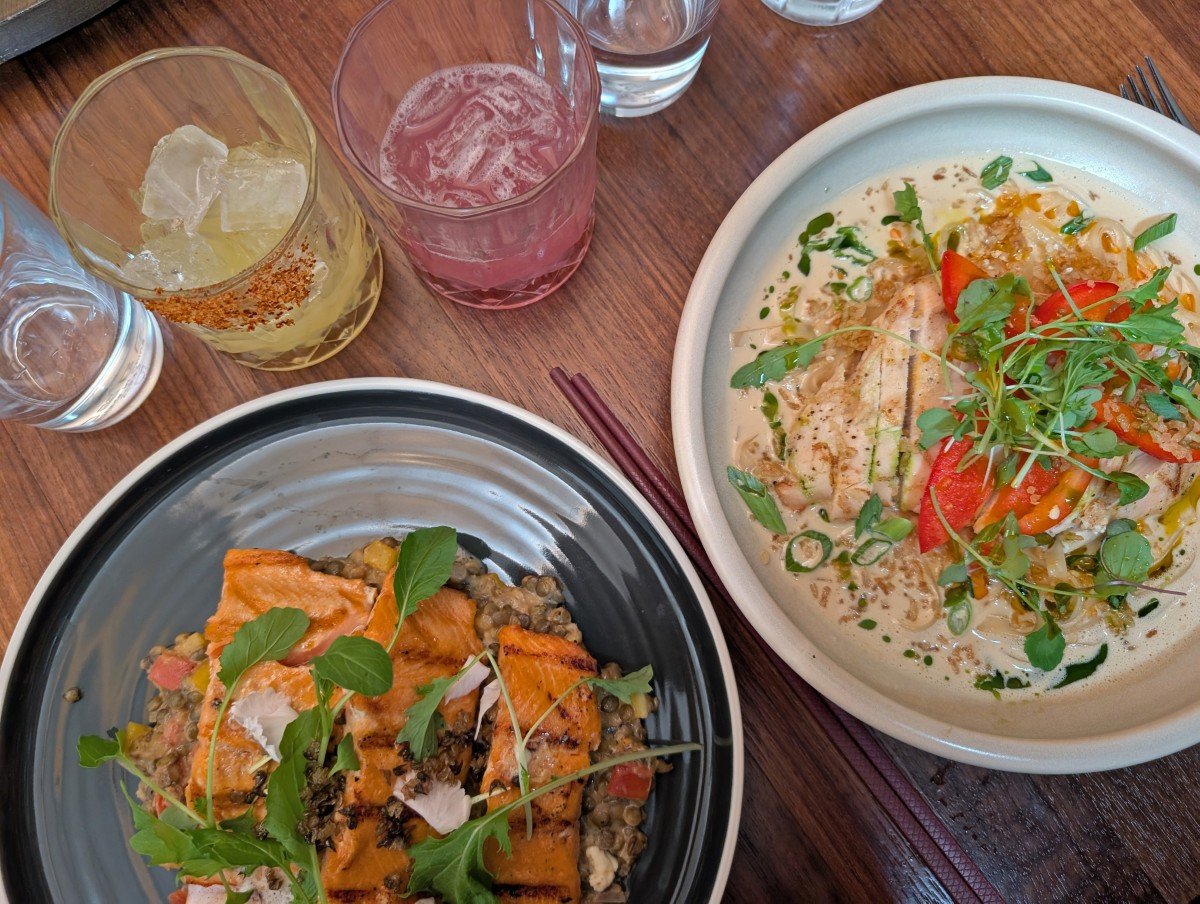 Overhead view of two colourful dishes at Loqui restaurant in Saskatoon, with two brightly coloured cocktail glasses above