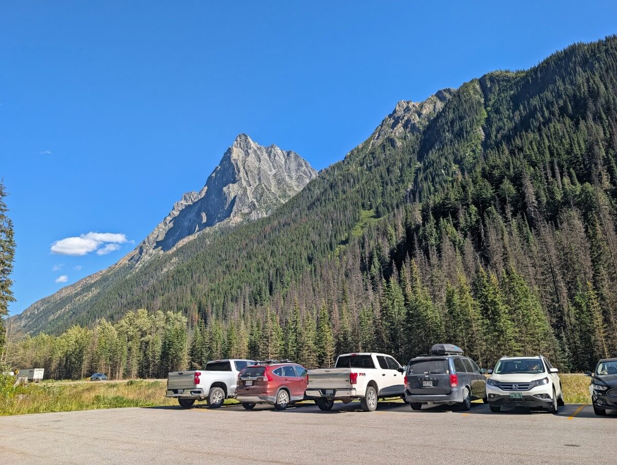 Hermit Trail parking area, with well spaced vehicles parked in lot, infront of mountain slope covered in trees