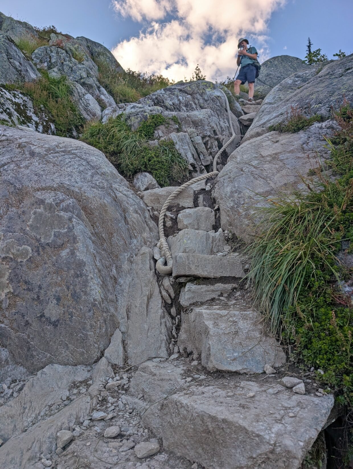 Looking up at steep section of the Hermit, which features rock steps and a rope. A hiker stands at the top taking a photo