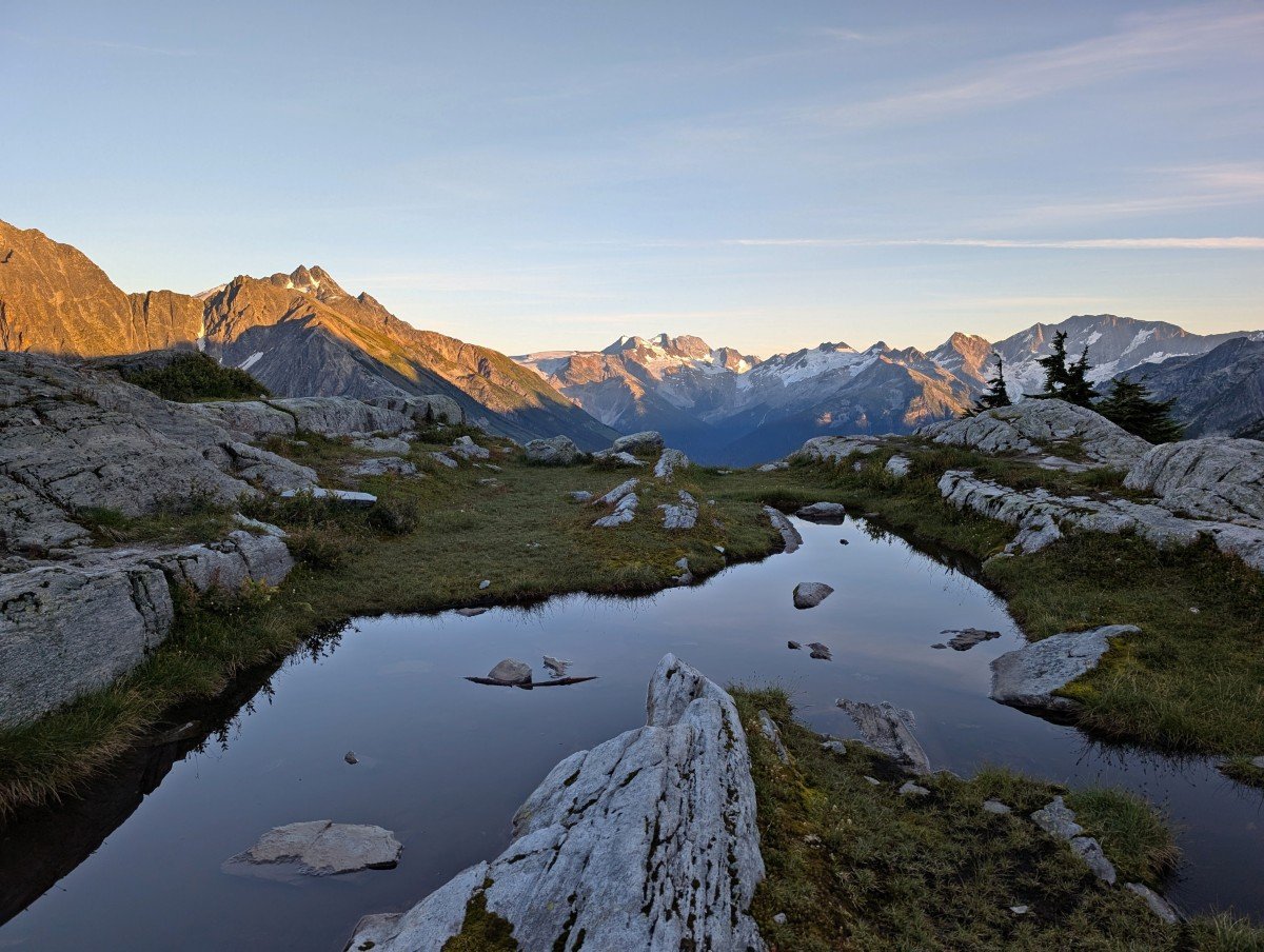 Alpine meadows view on Hermit Trail with tarn pools, rocks and snow capped mountain backdrop at sunset