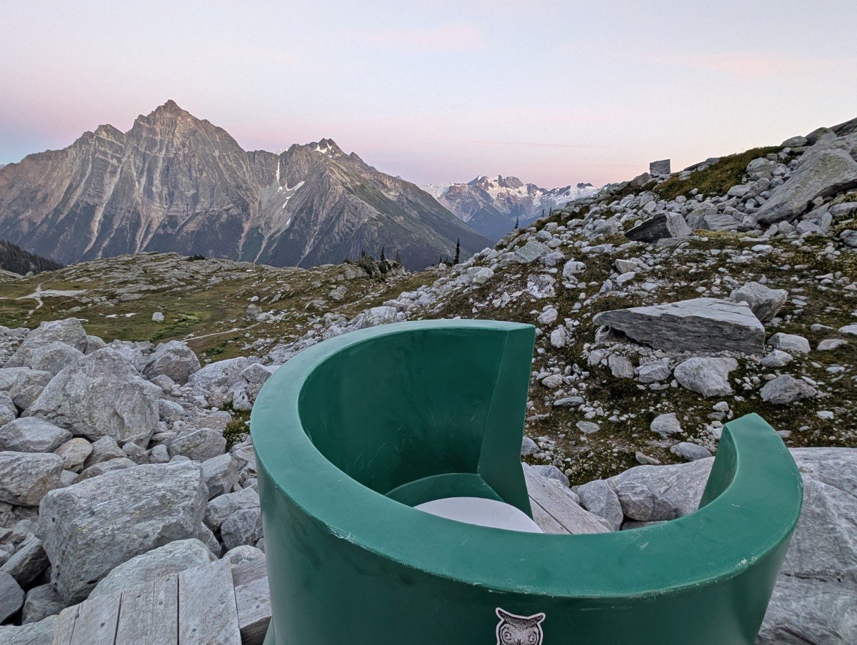 Close up of open sided green toilet throne at Hermit Meadows campground with alpine scenery in background at sunrise