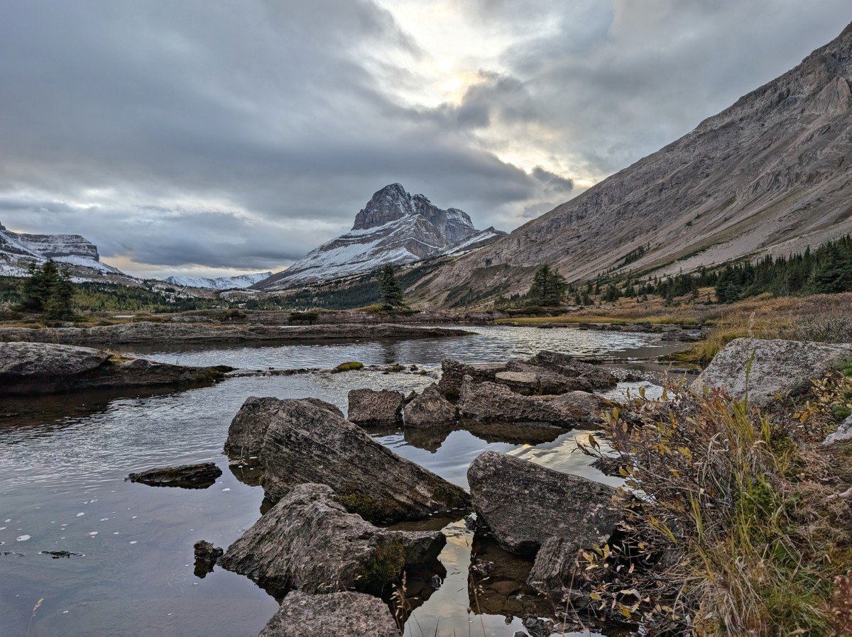 Creek view of Baker Lake with scattered rocks in foreground and snow capped mountains in background