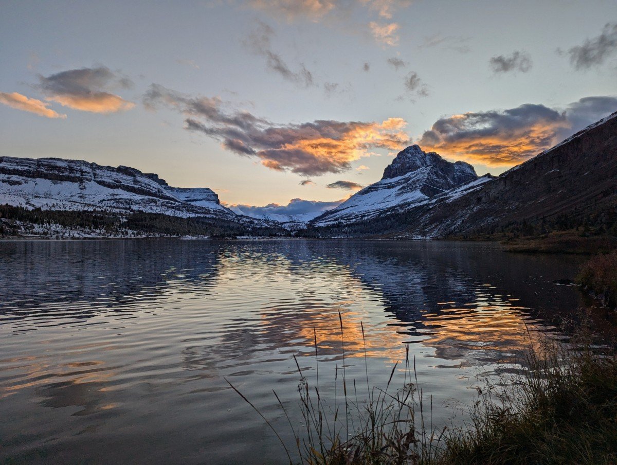 Shoreline view of Baker Lake at sunset with orange colours in the sky and clouds. The lake is reflective