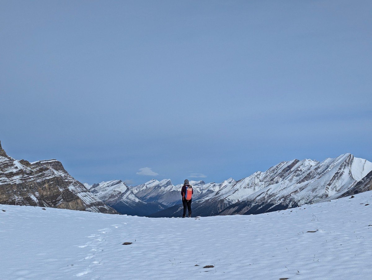 Back view of hiker standing on the top of Deception Pass on the Skoki Loop, with backdrop of snow covered mountains